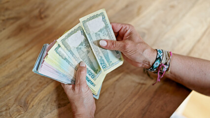 Middle age hispanic woman counting bangladesh taka banknotes at home