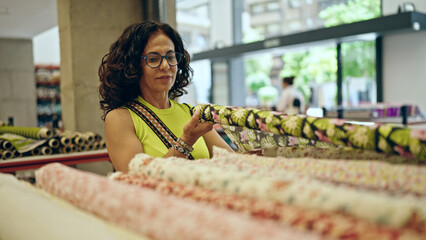 Middle age hispanic woman shopping fabrics at textile shop
