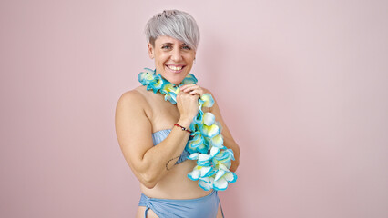 Young woman tourist wearing bikini and hawaiian lei smiling over isolated pink background