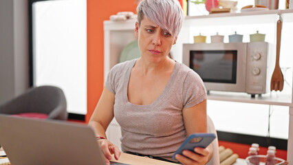 Young woman using laptop and smartphone with serious face at dinning room