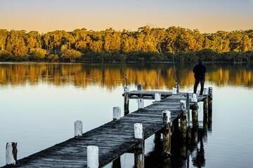 Man standing on a wooden pier overlooking a tranquil lake, getting ready to fish