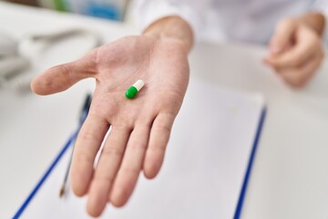 Young caucasian man doctor holding pill at clinic