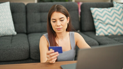 Young beautiful hispanic woman shopping with laptop and credit card sitting on floor at home