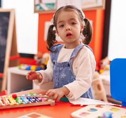 Adorable hispanic girl playing xylophone sitting on table at kindergarten