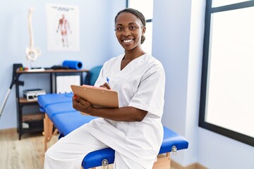 African american woman physiotherapist smiling confident writing medical report at rehab clinic