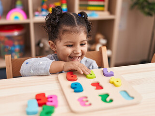 Adorable hispanic girl playing with maths puzzle game sitting on table at kindergarten