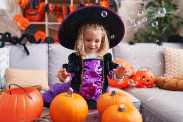 Adorable blonde girl wearing witch costume playing with soap bubbles at home
