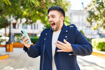 Young hispanic man using smartphone with surprise expression at park
