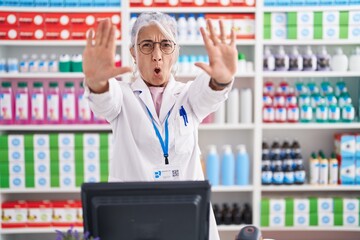 Middle age woman with tattoos working at pharmacy drugstore doing stop gesture with hands palms,...