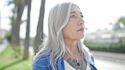 Middle age grey-haired woman looking to the side with serious expression at park