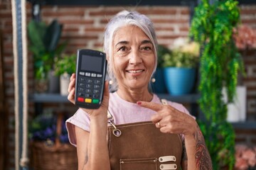Middle age woman with tattoos working at florist shop holding dataphone smiling happy pointing with...
