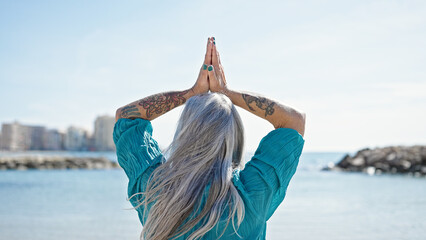 Middle age grey-haired woman doing yoga exercise at beach