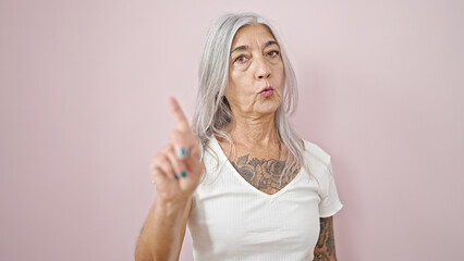 Middle age grey-haired woman saying no with finger over isolated pink background