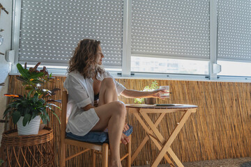 Young caucasian woman in a white shirt sitting on a balcony with closed roller shutters