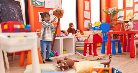 Adorable hispanic girl playing with horse toy at kindergarten