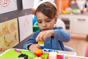 Adorable hispanic boy playing with construction blocks sitting on table at kindergarten