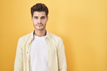 Young hispanic man standing over yellow background relaxed with serious expression on face. simple and natural looking at the camera.