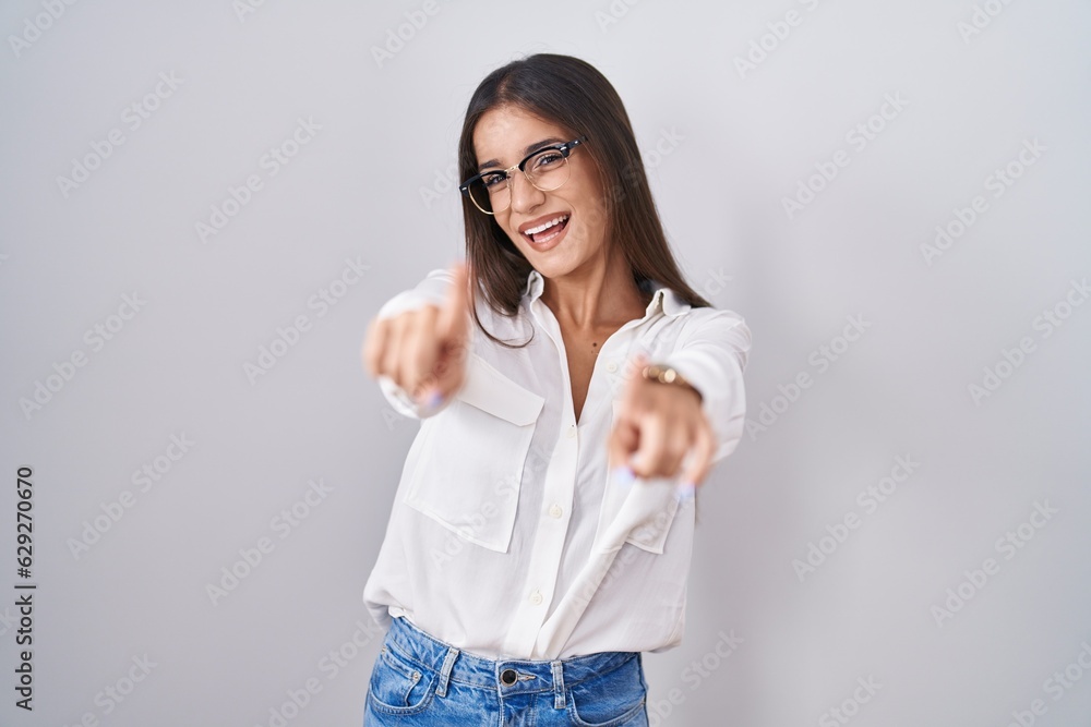 Poster young brunette woman wearing glasses pointing to you and the camera with fingers, smiling positive a