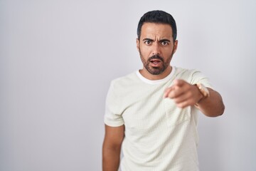 Hispanic man with beard standing over isolated background pointing displeased and frustrated to the...