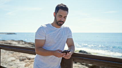 Young hispanic man using smartphone at seaside