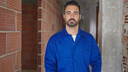 Fototapeta premium Young hispanic man worker standing with serious face at construction site