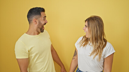 Man and woman couple standing together surprised over isolated yellow background