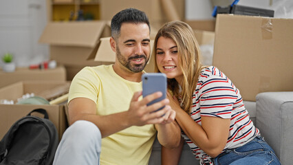 Man and woman couple sitting on floor using smartphone smiling at new home