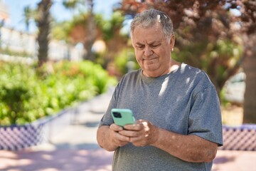 Fototapeta premium Middle age grey-haired man using smartphone with relaxed expression at park
