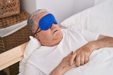 Middle age grey-haired man wearing sleep mask lying on bed sleeping at bedroom