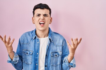 Non binary person standing over pink background crazy and mad shouting and yelling with aggressive expression and arms raised. frustration concept.