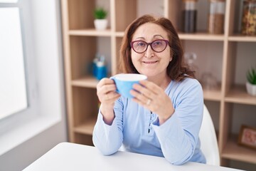 Senior woman drinking coffee sitting on table at home