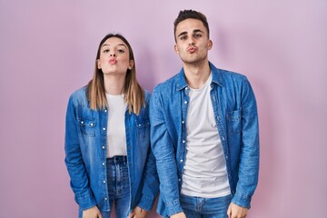 Young hispanic couple standing over pink background looking at the camera blowing a kiss on air being lovely and sexy. love expression.