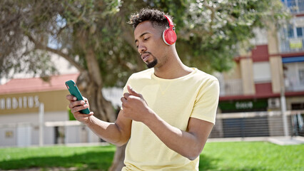 African american man listening to music using smartphone with thumb up at park