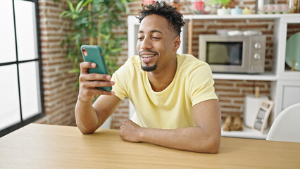 African american man using smartphone sitting on table at dinning room