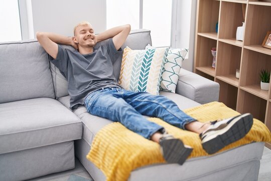 Young caucasian man relaxed with hands on head lying on sofa at home