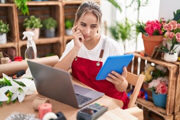 Young blonde woman florist using laptop and touchpad at flower shop