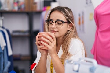 Young blonde woman tailor smiling confident drinking coffee at clothing shop