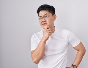 Young asian man standing over white background thinking worried about a question, concerned and nervous with hand on chin