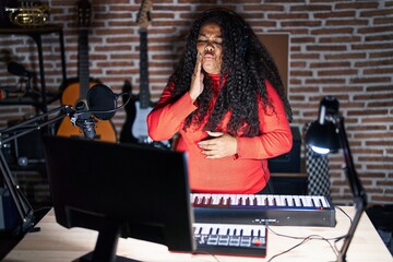 Plus size hispanic woman playing piano at music studio touching mouth with hand with painful expression because of toothache or dental illness on teeth. dentist