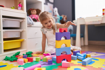 Adorable blonde girl playing with construction blocks sitting on floor at kindergarten