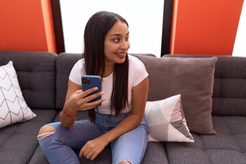 Young arab woman using smartphone sitting on sofa at home