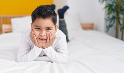 Adorable hispanic boy smiling confident lying on bed at bedroom