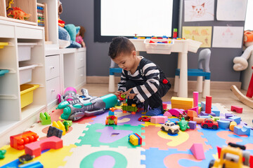 Adorable hispanic boy playing with car toy sitting on floor at kindergarten