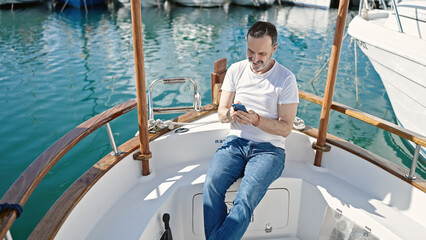 Middle age man using smartphone sitting on boat at port