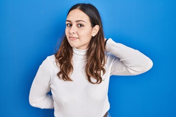 Obraz premium Young hispanic woman standing over blue background suffering of neck ache injury, touching neck with hand, muscular pain