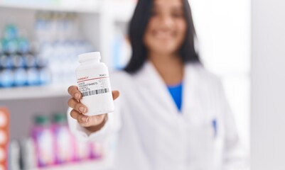 Young hispanic woman pharmacist smiling confident holding pills bottle at pharmacy