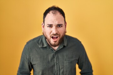Obraz premium Plus size hispanic man with beard standing over yellow background afraid and shocked with surprise and amazed expression, fear and excited face.
