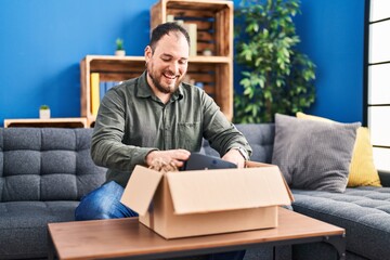 Young hispanic man unpacking virtual reality glasses sitting on sofa at home