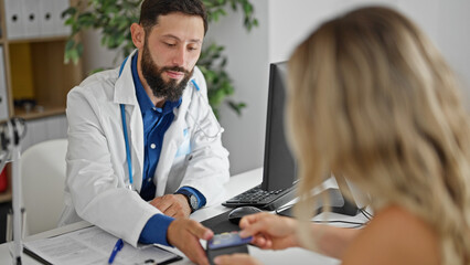 Young hispanic man doctor charging medical consultation to patient at the clinic