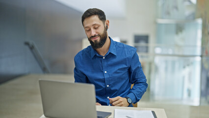 Young hispanic man business worker listening to music dancing at the office